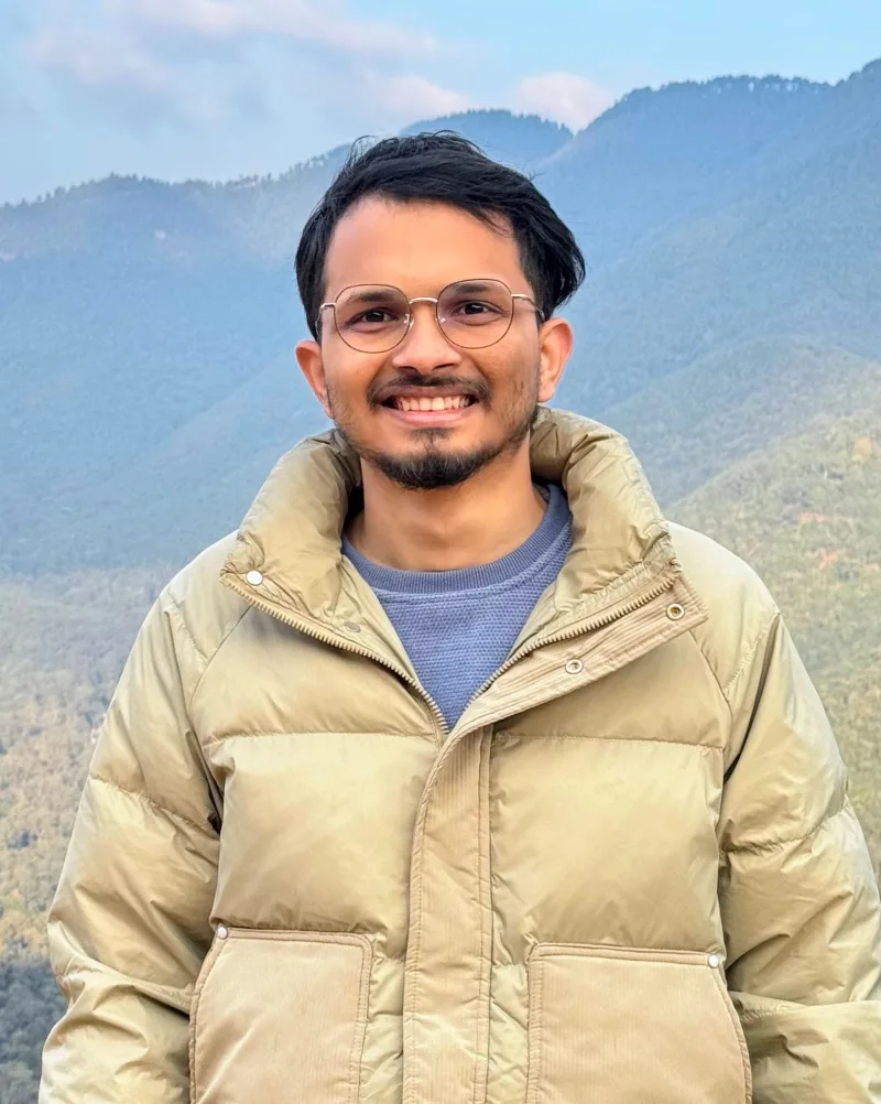 Anish Wagle, smiling, in front of forested hills in Nepal